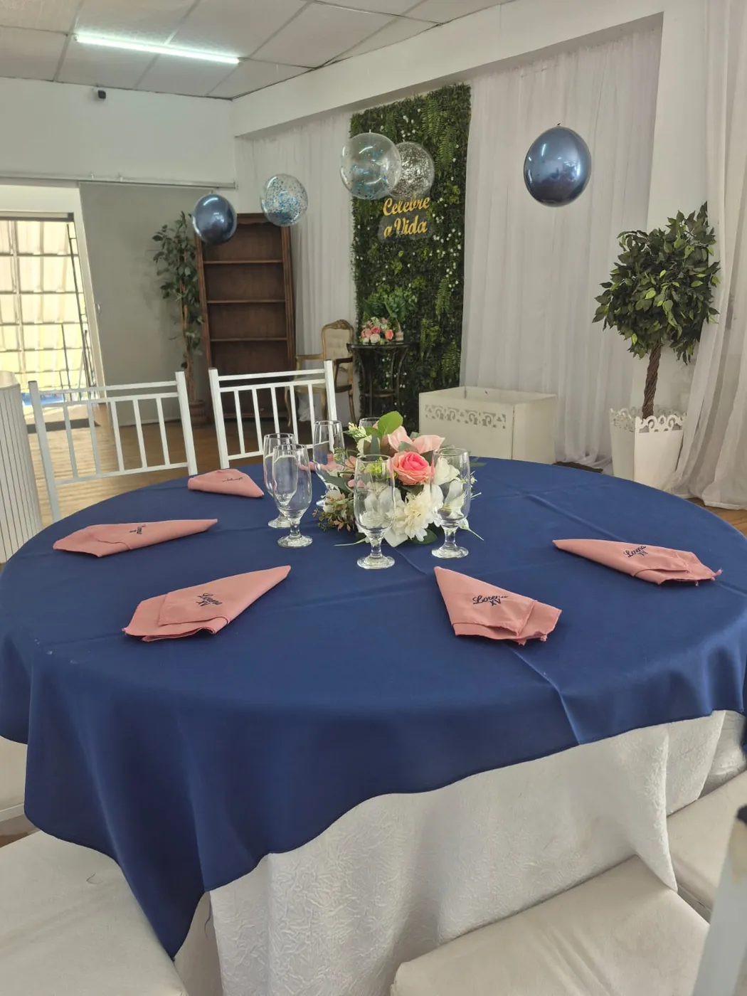 Mesa de convidados com toalha azul marinho, taças e arranjo de flores