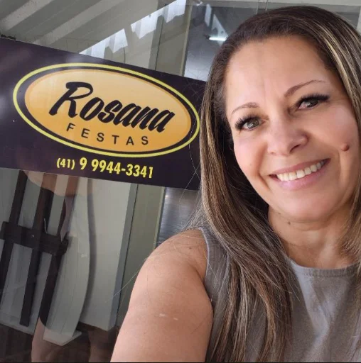 Rosana sorrindo em frente à placa da Rosana Festas